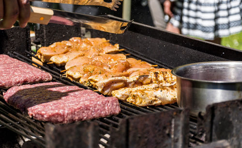 Close-up of man holding utensil and grilling meat in back yard.