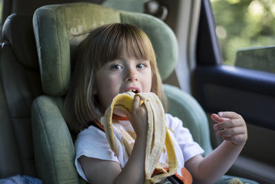 Portrait of cute girl eating a banana in car seat