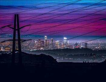 Electricity pylon in city against sky at night