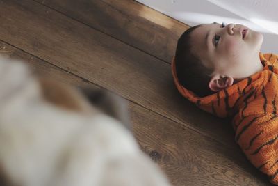 High angle view of cute boy looking away while lying on hardwood floor at home