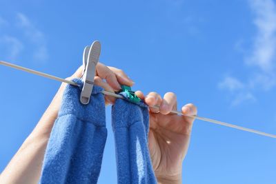 Cropped hands drying socks on clothesline against blue sky during sunny day