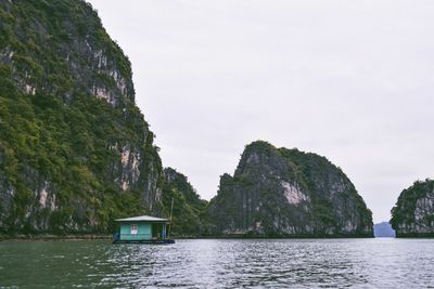 Houseboat by mountain in halong bay against clear sky