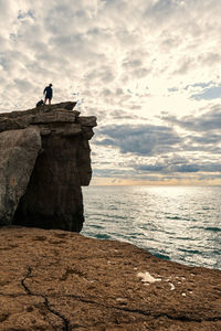 Man standing on rock by sea against sky