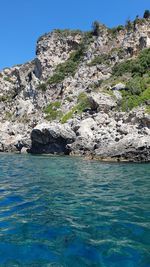 Rock formations by sea against clear blue sky