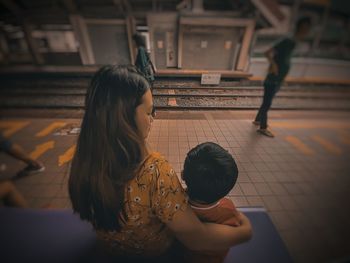 Rear view of woman sitting with son on railroad station platform