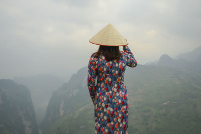Rear view of woman wearing conical hat while looking at mountain range 