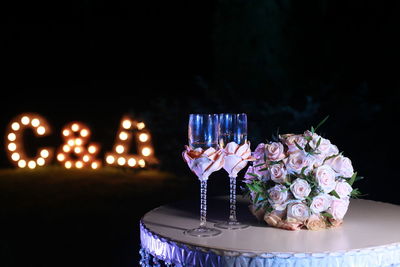 Flowers by champagne flutes on table at night