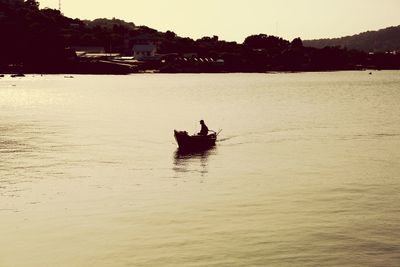 Silhouette person in boat on sea against sky