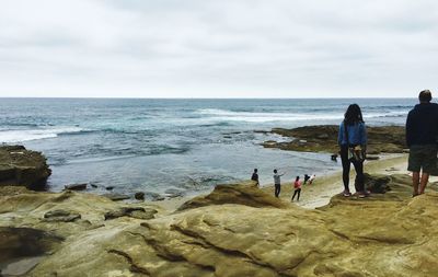 Rear view of people walking on beach against sky