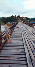 Side view of woman sitting on railroad track against sky