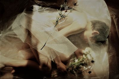 High angle view of naked boy holding flowers while lying with bubble wrap on floor