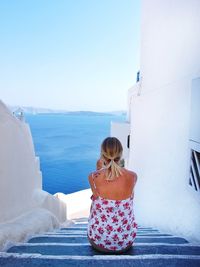 Rear view of woman sitting on steps by sea against clear sky