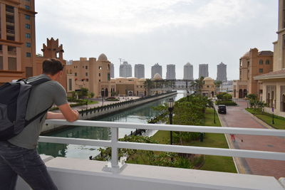 Rear view of man standing by swimming pool against buildings in city