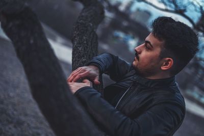 Portrait of young man looking at tree trunk