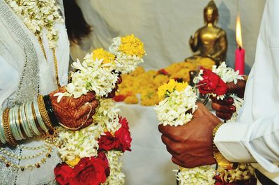 Midsection of bride and bridegroom holding floral garlands during wedding ceremony