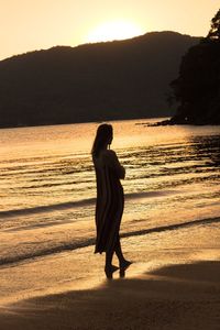 Rear view of woman looking at sea during sunset