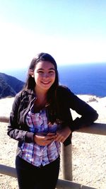 Portrait of smiling young woman standing at beach against clear sky