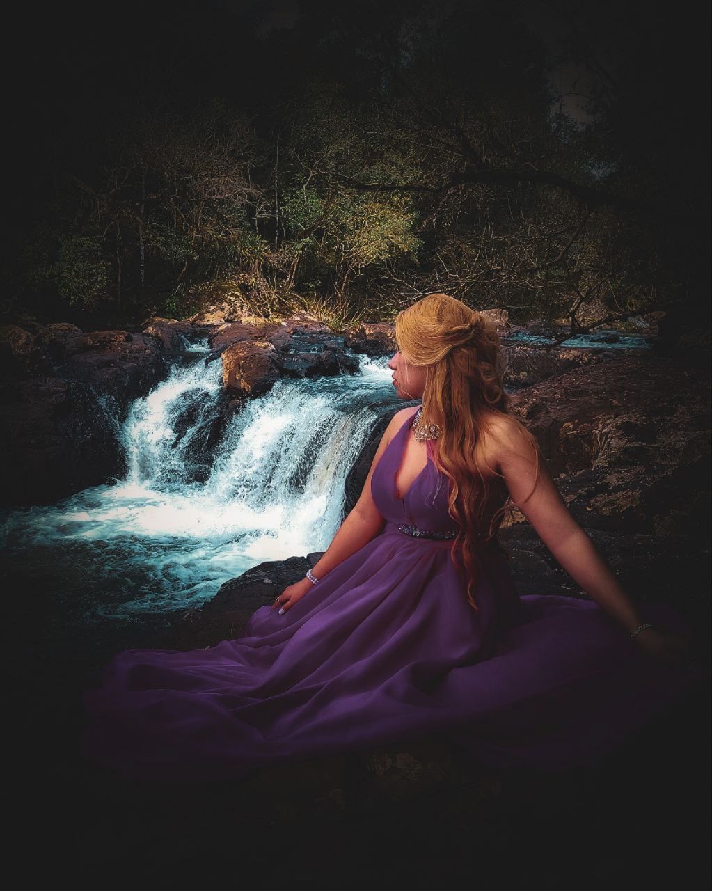 one person, darkness, women, long hair, hairstyle, young adult, adult, water, nature, dress, waterfall, motion, clothing, fashion, land, full length, light, lifestyles, flowing, sunlight, blond hair, outdoors, female, beauty in nature, tree, redhead, sitting, leisure activity, person, plant, portrait, tranquility