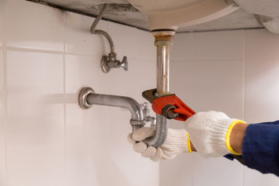 Close-up of hand holding faucet in bathroom