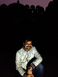 Portrait of man sitting against black background
