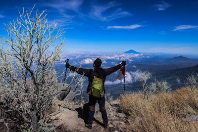 Rear view of man standing on mountain against blue sky