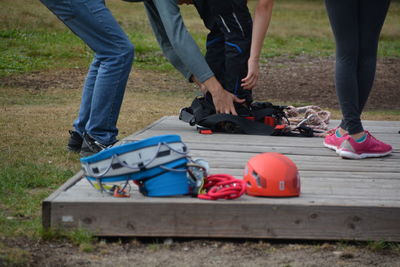 Low section of man assisting friend in wearing harness on field