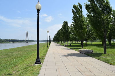 Walkway by trees against sky