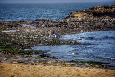 People standing on rock by sea against sky