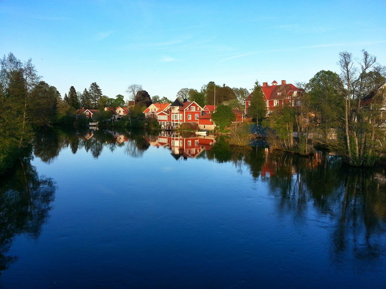 water, tree, reflection, clear sky, built structure, architecture, building exterior, waterfront, blue, lake, house, tranquility, tranquil scene, sky, nature, river, standing water, copy space, beauty in nature, scenics