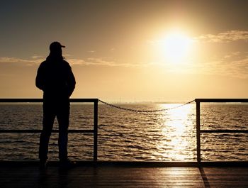 Adult tall man on pier board look over sea to morning sun. smooth water in bay. vignetting effect.