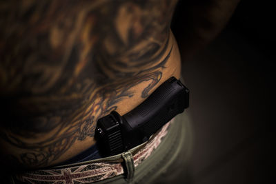 Midsection of tattooed man with gun in darkroom