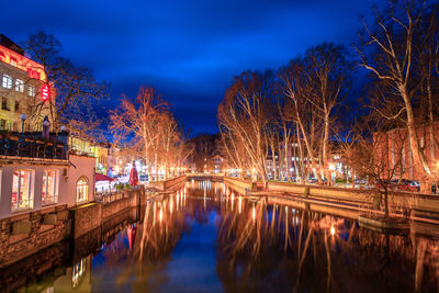 Illuminated buildings by river against sky at night