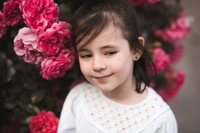 Closeup portrait of cute smiling kid girl 4-5 year old posing in blooming pink roses. summer season