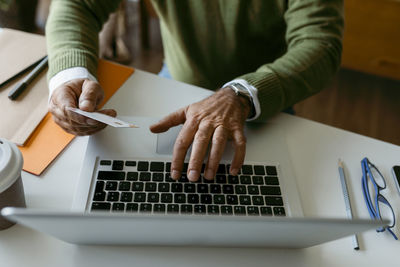 Midsection of man using credit card while working on laptop at home