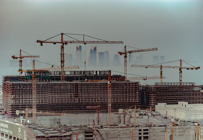 Cranes at construction site in city against sky