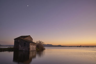 Building by lake against clear sky during sunset