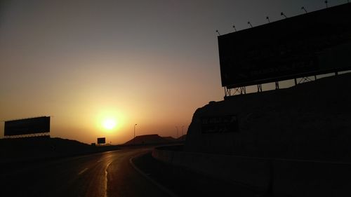 Road by city against sky during sunset