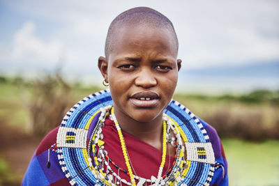 Portrait of woman wearing necklace standing against sky