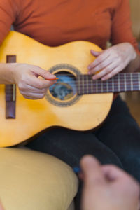 Midsection of woman playing guitar in home