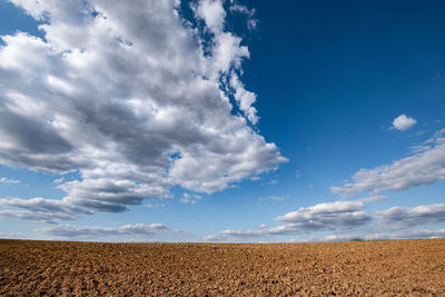 Scenic view of bare field under blue sky with dramatic clouds