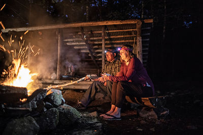 Couple enjoy warmth from campfire at appalachian trail lean to, maine