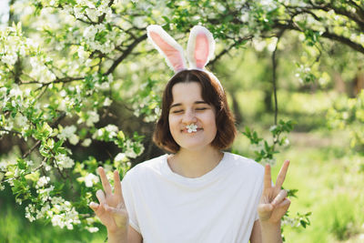 Funny teen girl with bunny ears on easter egg hunt in sunny spring garden