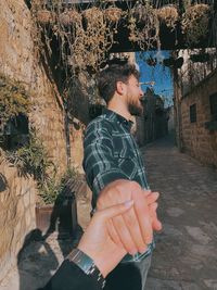 Young man looking away while standing against tree