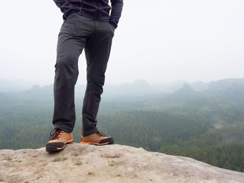 Low section of man standing on mountain against sky