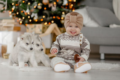 Cute baby girl sitting on floor with puppies of husky at home with christmas decorations 