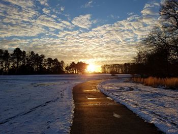 Snow covered road against sky during sunset