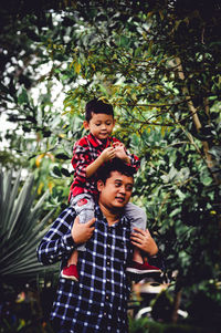 Father and son standing by tree against plants