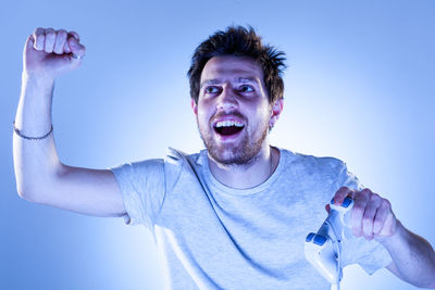 Portrait of young man with arms raised against blue sky