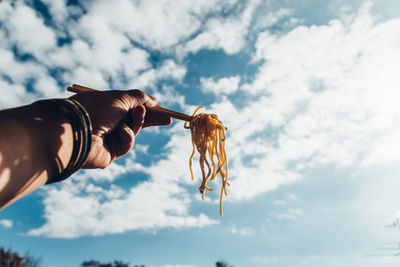 Cropped hand holding noodles against sky