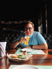 Portrait of man holding drink by food in cafe